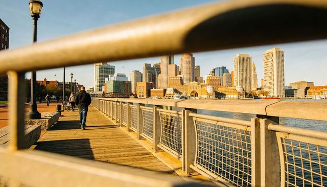 Sunlit urban waterfront boardwalk with pedestrians walking toward city skyline