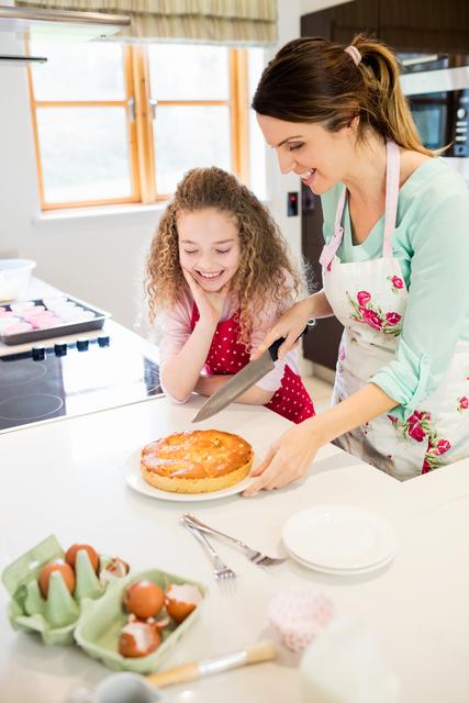 Mother and daughter enjoying quality time together in the kitchen, cutting a freshly baked cake. Perfect for illustrating family bonding, home cooking, and domestic life. Ideal for use in parenting blogs, cooking websites, family-oriented advertisements, and lifestyle magazines.