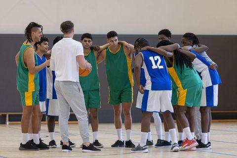 Diverse Male Basketball Team Huddling with Coach on Court