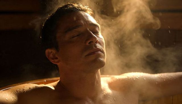 Reclining man relaxing in wooden hot tub with steam, amber glow and spa serenity