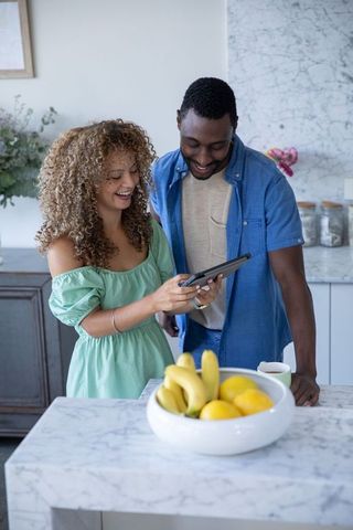 Multicultural couple sharing tablet in modern marble kitchen, smiling and connecting