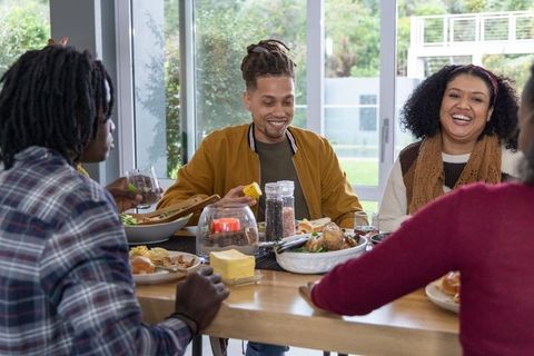 Friends laughing and sharing dinner around sunlit dining table with corn and salad