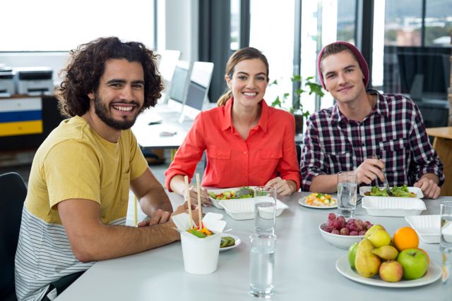 Group of business colleagues enjoying lunch together in a bright, modern office. Perfect for illustrating corporate culture, teamwork, office environments, social company events, healthy eating in the workplace, and team bonding sessions.