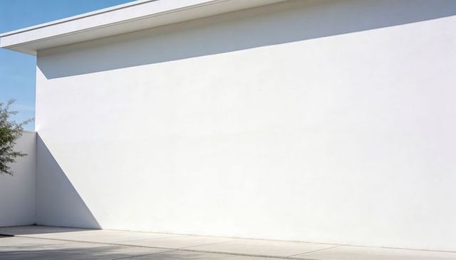 Minimalist white plaster wall casting triangular shadow with flat roof overhang
