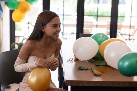 Happy young woman arranging gold balloons amidst festive setting