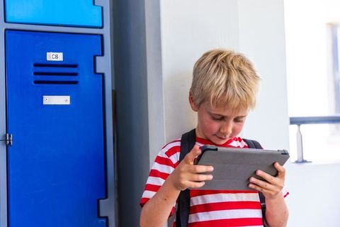 Schoolboy using tablet by blue locker in hallway, digital learning and student focus