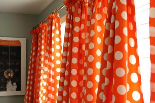 Bright orange polka dot curtains hang on a window, adding a cheerful and lively touch to the room. Sunlight filters through the curtains, creating a warm and inviting atmosphere. Ideal for home decor themes focusing on playful, energetic design elements. Perfect for promoting window treatments, curtain fabrics, or home styling ideas.