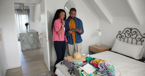 Couple Using Tablet While Packing Suitcase for Relaxing Vacation