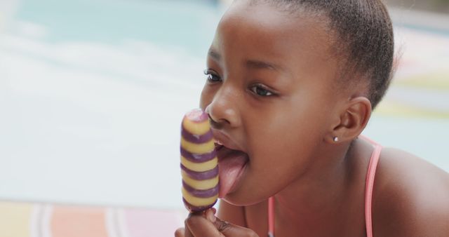 Happy african american girl eating ice cream at pool in sunny garden. Lifestyle, free time, nature, childhood and domestic life, unaltered.