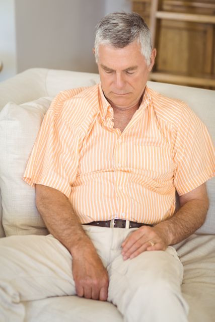 Senior man taking a nap on a comfortable sofa in a living room. Ideal for use in articles or advertisements related to senior lifestyle, relaxation, home comfort, or health and wellness.