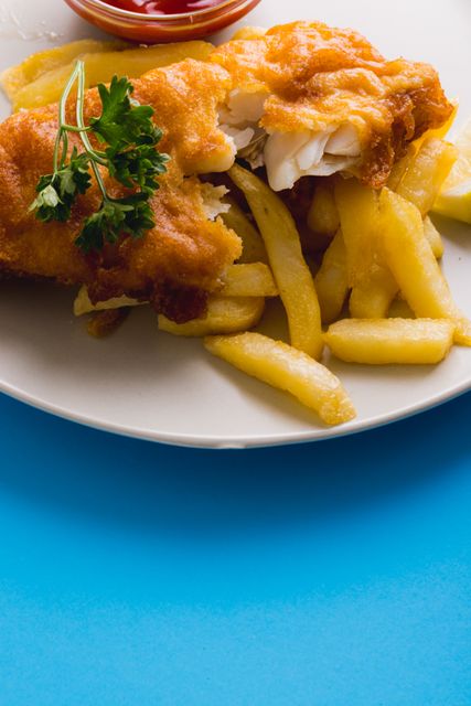 This image shows a close-up of fried fish and french fries on a plate with a side of ketchup. The dish is garnished with parsley and set against a blue background. Ideal for use in food blogs, restaurant menus, fast food advertisements, and culinary websites.