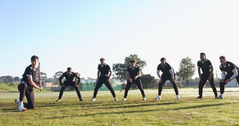 Cricket team practicing on grass field in black uniforms