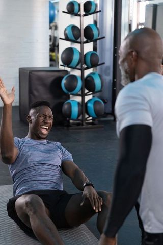 African american trainer coaching client during core workout on mat with medicine balls