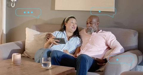 Cuddling couple relaxing and scrolling smartphone on sofa, cozy intimate moment