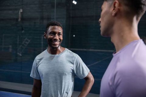 Smiling diverse male training partners talking and cooling down on indoor glass court