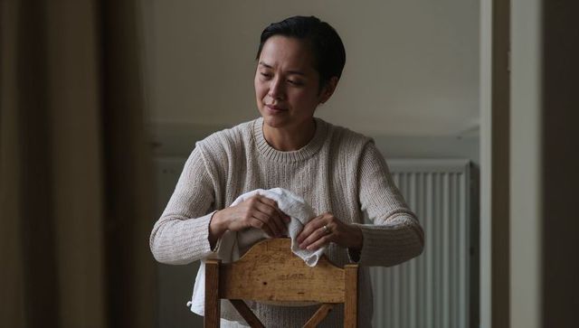 Leaning woman holding cloth over chair back in serene minimalist beige interior, thoughtful