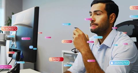Asian man holding eyeglasses leaning toward monitor with analytics overlays in office