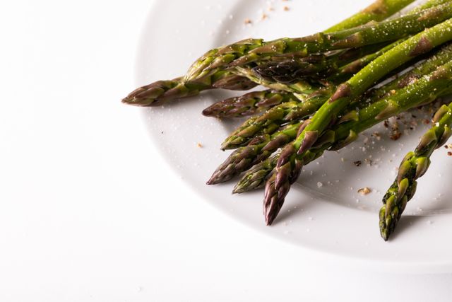 Close-up of fresh asparagus spears on a white plate with a white background. Ideal for use in articles or advertisements related to healthy eating, organic food, vegetarian recipes, or culinary presentations. The clean and minimalistic background makes it perfect for adding text or logos.