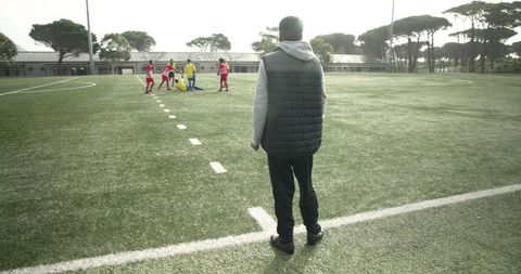 Soccer Coach Watching Players Practice on Sunny Field