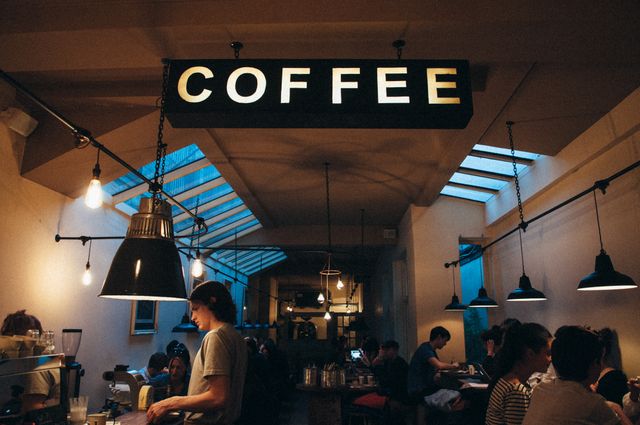 Cozy coffee shop interior with modern lighting features a warm ambiance where patrons are seen socializing and enjoying their time. Ideal for themes focused on social gatherings, urban lifestyles, and casual dining experiences.