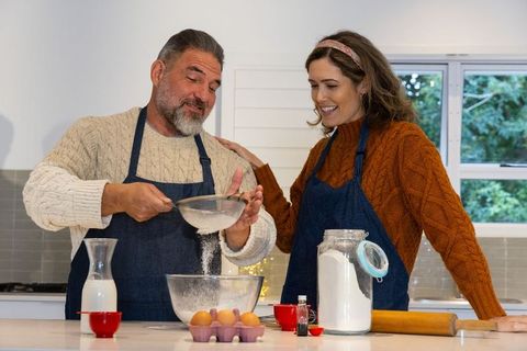 Middle-aged couple baking together, sifting flour at cozy kitchen island, sharing joy