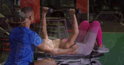 Personal trainer spotting woman during dumbbell bench press in gym