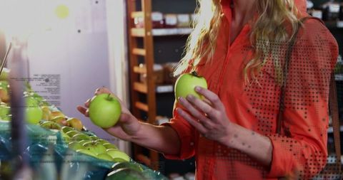 Selecting green apples while shopping at grocery produce display in bright orange shirt