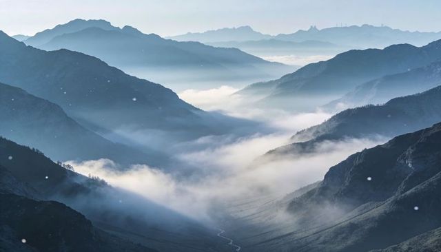 Misty Alpine Valley with Layered Ridgelines and Winding Stream Under Drifting Fog