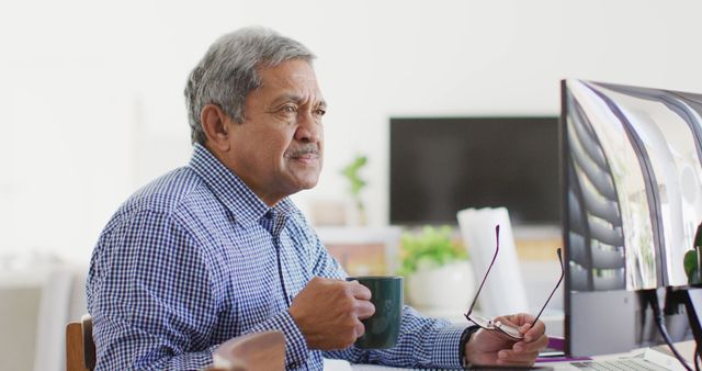 Image of senior biracial man sitting at desk drinking coffee and using computer at home - Download Free Stock Photos Pikwizard.com