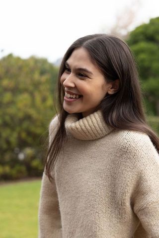 Smiling young woman wearing beige chunky turtleneck sweater in garden portrait