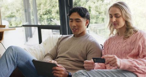 Couple shopping online together on tablet holding credit card on cozy living couch
