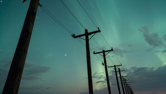 Wooden utility poles receding across rural plain under green aurora night sky