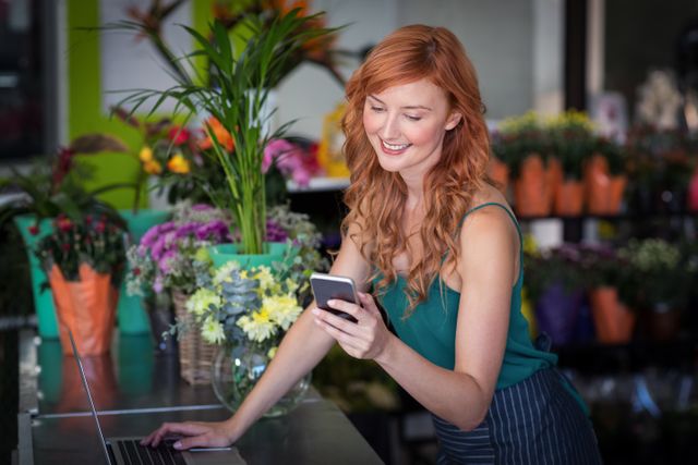 Female florist using mobile phone while using laptop in flower shop