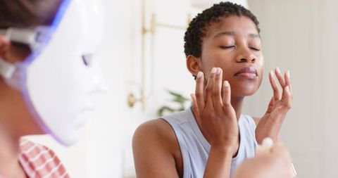 African american friends applying skincare at home vanity with led mask and moisturizer