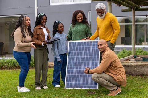 Multigenerational family inspecting solar panel with technician on modern home lawn