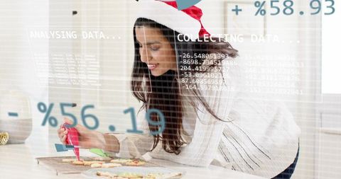 Woman in santa hat decorating christmas cookies with icing and digital data overlays