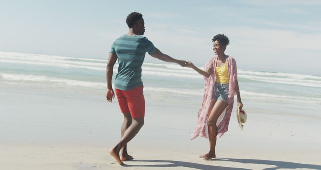 Happy african american couple walking and holding hands on sunny beach - Download Free Stock Photos Pikwizard.com