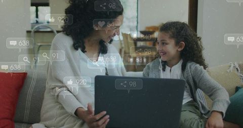 Mother and daughter sharing laptop and smiling on cozy sofa while learning together