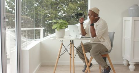 Black content creator recording podcast at minimalist home workspace with laptop and mic