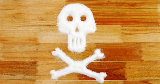 A skull and crossbones symbol made from sugar on a wooden surface, warning about the dangers of excessive sugar consumption. It creatively conveys the message that sugar can be harmful to health.