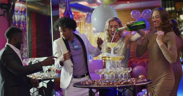 Image of happy caucasian woman pouring a champagne fountain with diverse friends at nightclub. Fun, drinking, going out and party concept.