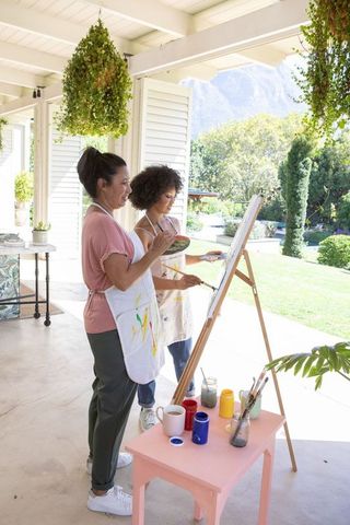 Mother Daughter Duo Painting on Veranda Surrounded by Greenery
