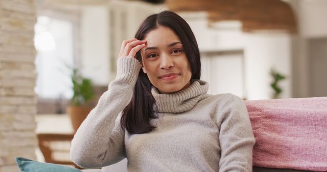Woman relaxing indoors wearing cozy sweater, sitting comfortably on sofa. Ideal for lifestyle, fashion, and home decor concepts, highlights warmth and comfort. Great for promoting cozy clothing lines, lifestyle blogs, and relaxation tips.