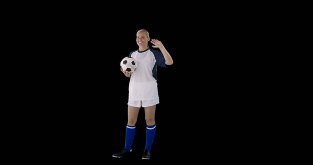 A female soccer player dressed in a white and blue uniform is waving and smiling while holding a soccer ball. The black background creates a sharp contrast, making her stand out. The image can be used for promoting sports events, athletic apparel, training programs, soccer team advertisements, and youth sports initiatives.