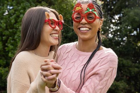 Multiracial friends laughing while holding hands in festive novelty glasses and sweaters