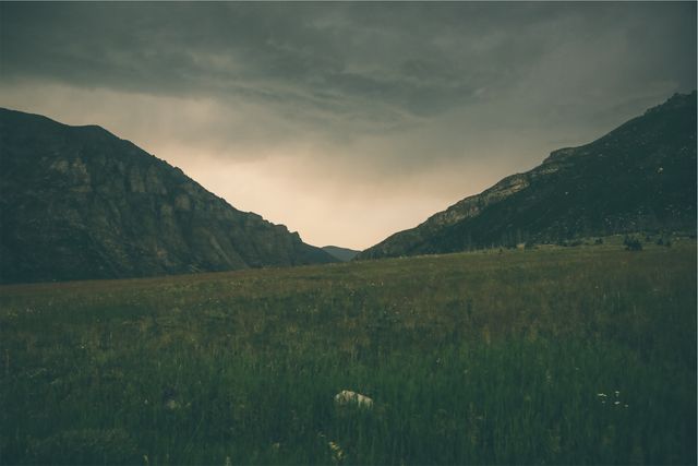 Dark clouds hover over a serene mountain valley as dusk approaches, creating a dramatic and moody atmosphere. Ideal for use in travel blogs, nature magazine articles, environmental campaigns, or outdoor adventure promotions.