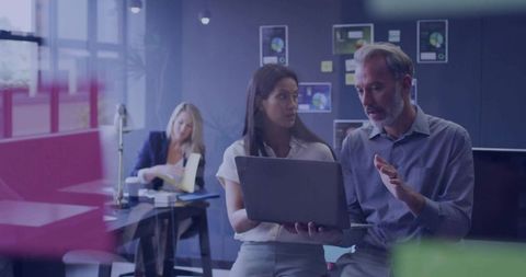 Collaborating professionals reviewing laptop data and strategy in modern glass office