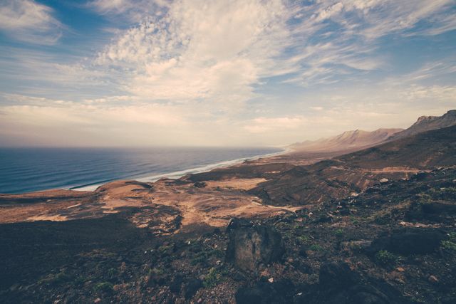 Expansive view capturing a rugged coastline with mountains extending into horizon. Dramatic sky with scattered clouds adds depth and beauty. Ideal for backgrounds, travel blogs, nature magazines, or environmental campaigns highlighting natural beauty and preservation.