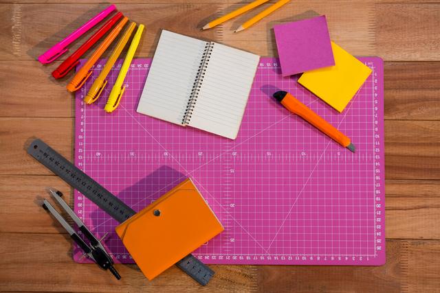Colorful school supplies arranged on wooden table, including notebook, pencils, ruler, sticky notes, and cutting mat. Ideal for educational content, back-to-school promotions, and organizational tips.