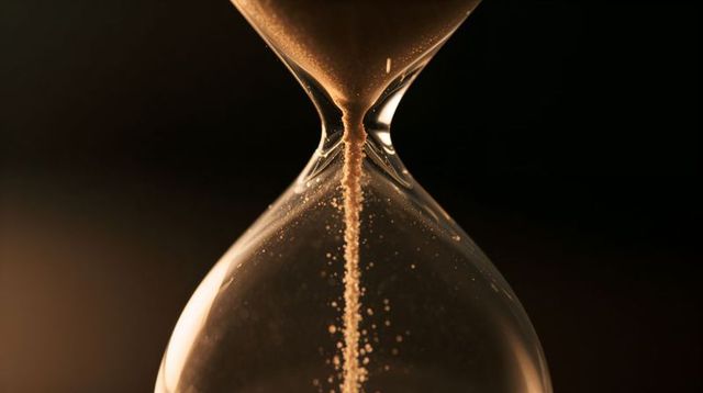 Golden sand pouring through glass hourglass macro close-up evoking time passing conceptual